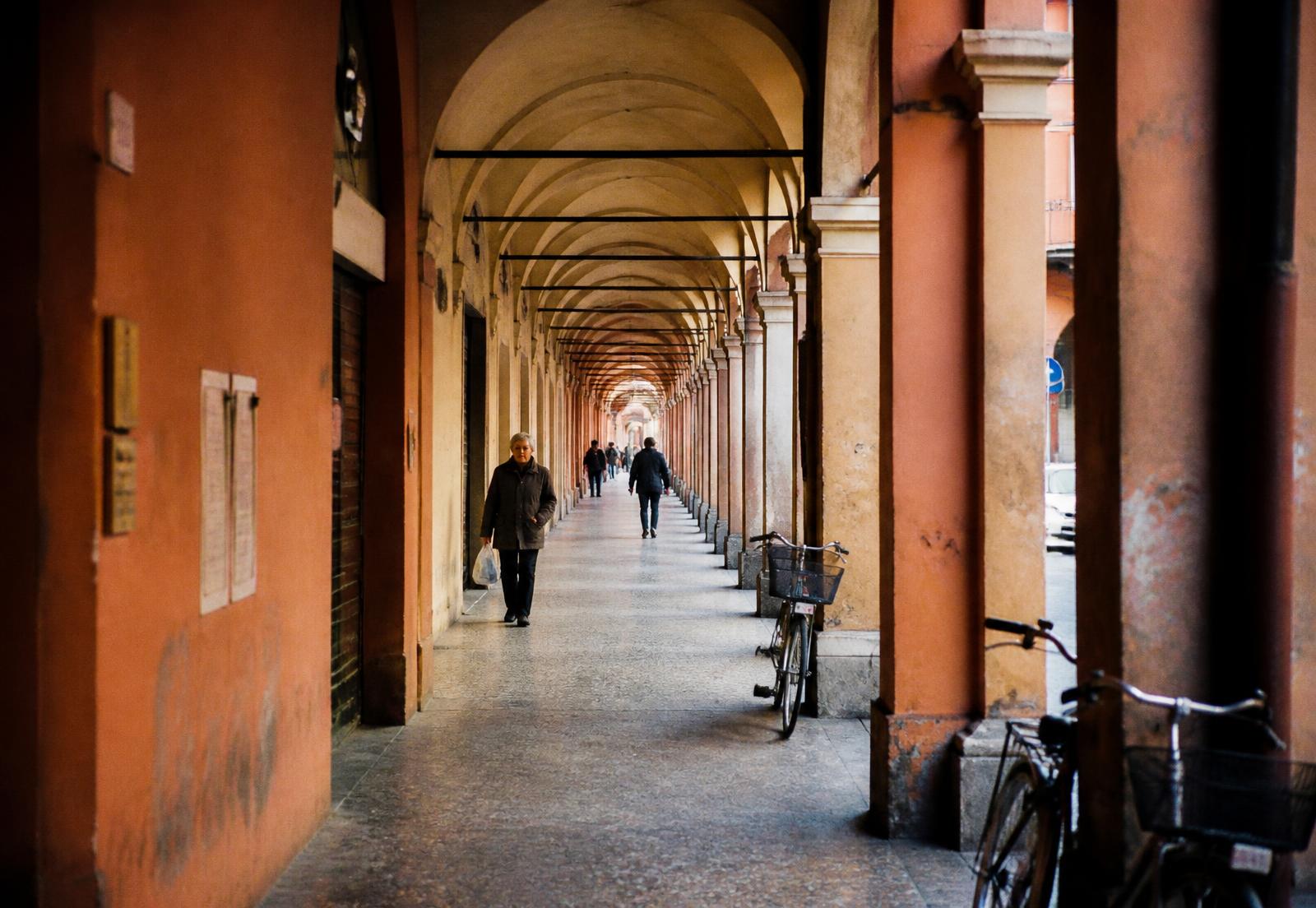 Portici di Bologna, arcate in ocra e terracotta con biciclette e passanti